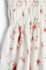 Vestido corto de popelina de algodón color blanco con estampado floral en tonos rosados. Tiene escote cuadrado con elástico, mangas cortas abullonadas con elástico y cuerpo fruncido.