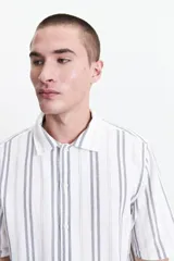 Camisa de manga corta con corte oversize, a rayas verticales blancas y grises, con cuello clásico y cierre frontal con botones. Confeccionada en algodón.