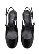 Zapato destalonado negro de efecto charol, con tacón bloque bajo y puntera redondeada. Presenta una tira fina con hebilla ajustable sobre el empeine.