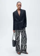 Pantalón largo de viscosa con estampado de cebra en blanco y negro, tiro medio, diseño recto y cierre frontal con botón, gancho y cremallera.