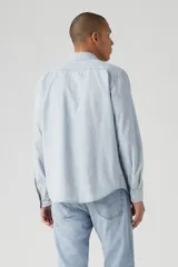 Camisa celeste a rayas verticales blancas, de corte recto, manga larga y bolsillo en el pecho.