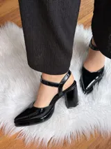 Sandalias negras de charol con punta fina, tira al tobillo con hebilla y tacón bajo.