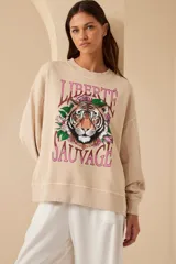 Buzo color beige de algodón con cuello redondo y mangas largas. Estampado frontal con un tigre, flores y la frase 'Liberté Sauvage'.