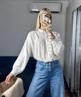 Camisa blanca de mangas largas con detalles de encaje en el cuello y en el frente.