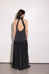 Vestido largo negro con finas líneas plateadas, de corte holgado, escote halter y espalda baja. Presenta volados en el cuello y en la cadera.