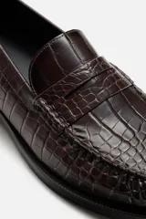 Mocasín de vestir color marrón oscuro con estampado de cocodrilo, horma redonda y suela con ligero tacón.