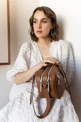 Bandolera rectangular de cuero color nude con doble compartimento con cierre de cremallera plateada y correa de cuero ajustable.