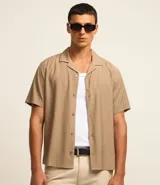 Pantalón de vestir color beige, de corte slim, con bolsillos laterales y traseros. Se ajusta a la cintura con cinturón de cuero negro.