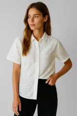 Camisa blanca de algodón con bordado tipo broderie, corte holgado, cuello camisero y cierre frontal con botones.
