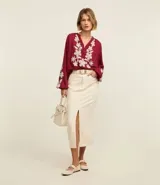 Blusa color borgoña de batista con cuello en V y botones. Presenta bordados florales blancos en el frente y las mangas largas con puños elásticos.