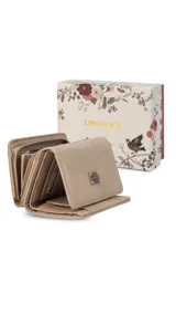 Billetera corta de símil cuero color beige claro, con cierre de broche a presión en la solapa principal. Presenta múltiples compartimentos internos para tarjetas y billetes, y un bolsillo exterior con cierre en la parte posterior. Lleva una placa metálica con el logo de la marca.