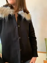 Cárdigan negro de lana merino con cuello de piel sintética gris. Tiene cierre frontal con botones.