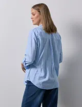 Camisa celeste de lino, con cuello con solapa, escote en V y abertura central con botones. Largo de manga regulable con presilla y botón. Delantera con bolsillo aplicado.