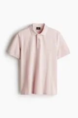 Chomba de piqué de algodón color rosado, de corte clásico, con cuello clásico, tapeta de botones y mangas cortas con terminación acanalada.