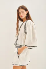 Camisa blanca de algodón con bordado negro en el ruedo, corte amplio y largo corto. Escote redondo y mangas largas abullonadas.