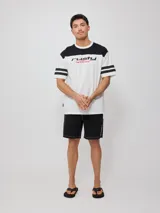 Remera blanca de hombre con corte negro en la parte superior del pecho y mangas cortas con tres rayas horizontales negras. Estampado frontal con el logo de Rusty en negro y la palabra 'Culture' en rojo.