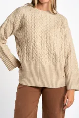 Sweater de punto color beige melange, con cuello redondo y tejido trenzado en el cuerpo y mangas. Presenta un borde inferior de punto acanalado.