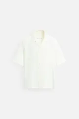 Camisa color crema de corte relaxed fit, confeccionada en tejido con mezcla de modal. Tiene cuello bowling, manga corta, bolsillo plastrón en el pecho y cierre frontal con botones.