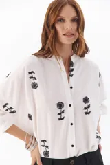 Camisa beige con bordado floral negro, de corte suelto y botones frontales.