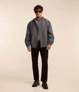 Campera gris con capucha, cuello alto, mangas largas y bolsillos con solapa y botones. Cierre frontal oculto. Marca Request, colección Primavera/Verano 2024.