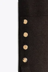 Jersey negro de punto liso con cuello alto, manga larga y detalle de botones dorados en los puños.