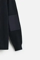 Sweater negro de punto con cuello redondo y manga larga. Presenta parches combinados a tono en hombros y codos.