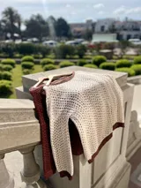 Sweater de punto calado color crema, con cuello, puños y ruedo en marrón con lurex. El cuello puede usarse de dos formas: mostrando un hombro o de forma clásica.