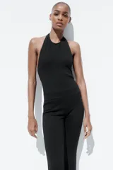 Mono largo negro de tejido elástico, con cuello halter, espalda descubierta y bajo acampanado.