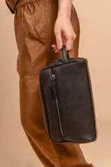 Neceser unisex de símil cuero color camel, con forma rectangular y asa lateral. Presenta un bolsillo frontal con cierre vertical y un compartimento principal con cierre superior.