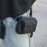 Riñonera negra con correa ajustable, confeccionada en material impermeable xPac X21. Cuenta con 7 bolsillos internos y 2 externos, organizador con apertura de 180°, espacio para cables y cargadores, detalles en color ladrillo y cierres impermeables.