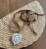 Collar con dije de león calado en color blanco y cordón de cuero marrón con cuenta dorada.