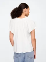 Blusa blanca de manga corta con escote en V y detalle de volados en el cuello.