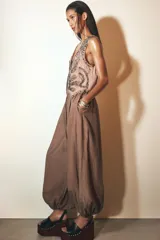 Pantalón bombacho marrón de tejido fluido, tiro medio con cintura elástica ajustable con cordones, bolsillos laterales ocultos y bajo abullonado con elástico interior.