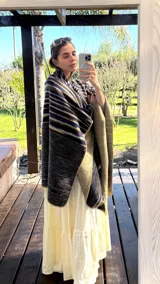 Ruana tejida con rayas horizontales en tonos azul, marrón y beige, con flecos en los bordes.