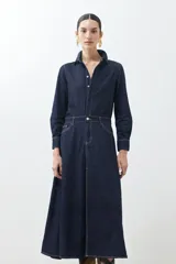 Vestido camisero de jean azul oscuro, corte evasé, largo midi, con cuello camisero, cierre frontal con botones, mangas largas con puños abotonados, bolsillos en el pecho y tajo lateral.