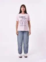 Remera blanca de algodón con cuello redondo y manga corta. Presenta un pequeño bordado en el pecho izquierdo con una figura que parece ser una persona acostada en una tabla de surf o flotador.