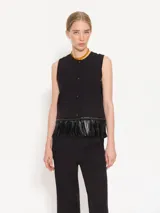 Chaleco negro corto de twill con ruedo terminado en flecos de cuerina al tono y acceso delantero mediante botones forrados con tela base.