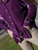 Camisa roja de terciopelo con cuello clásico, botones frontales y mangas largas con puños abotonados. Tiene dos bolsillos de parche en el pecho.