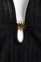 Vestido largo de punto pointelle negro con estilo crochet. Modelo entallado con escote halter en V y adorno de metal en forma de sol en el centro del busto. Falda sirena con bajo recto.