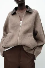 Chaqueta de punto color marrón claro con cuello solapa a contraste en simil cuero color marrón oscuro y manga larga. Cierre frontal con cremallera metálica.