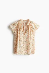 Blusa de tejido crepé color crema con estampado de flores pequeñas en tonos rosados y marrones. Tiene corte holgado, cuello con volados y escote en V con tiras para ajustar. Las mangas son cortas tipo mariposa con ribete de volado.