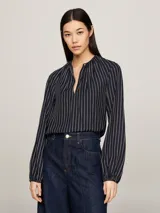 Blusa de viscosa con estampado de rayas verticales blancas sobre fondo azul marino, cuello redondo con abertura en V, cierre de lágrima en la parte delantera y mangas largas con puños fruncidos.