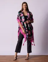 Kimono tejido con estampado floral en tonos rosados, celestes y verdes sobre fondo negro. Presenta terminación de ruedo con borlas rosadas y ribete fucsia.