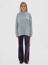 Buzo tejido color blanco, con cuello subido tipo polera, diseño oversized y largo con pequeños cortes laterales.