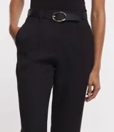 Pantalón de vestir negro de corte carrot, con cintura alta, trabillas y cinturón con hebilla metálica.