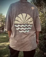 Remera marrón con efecto gastado, corte amplio y estampado en la espalda con un sol naciente sobre el mar.