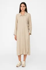 Túnica midi color beige de lino, corte holgado, manga larga, cuello camisero y cierre frontal con botones.
