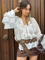 Blusa negra traslúcida con volados, mangas largas abullonadas y cierre frontal con botones.