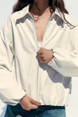 Chaqueta bomber color crudo con cuello solapa, manga larga con puño elástico interior, bolsillos laterales, forro interior, bajo acabado en elástico y cierre frontal con cremallera.