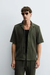 Camisa verde militar de corte relaxed fit, con cuello bowling, manga corta, bajo con aberturas laterales y cierre frontal de botonadura.